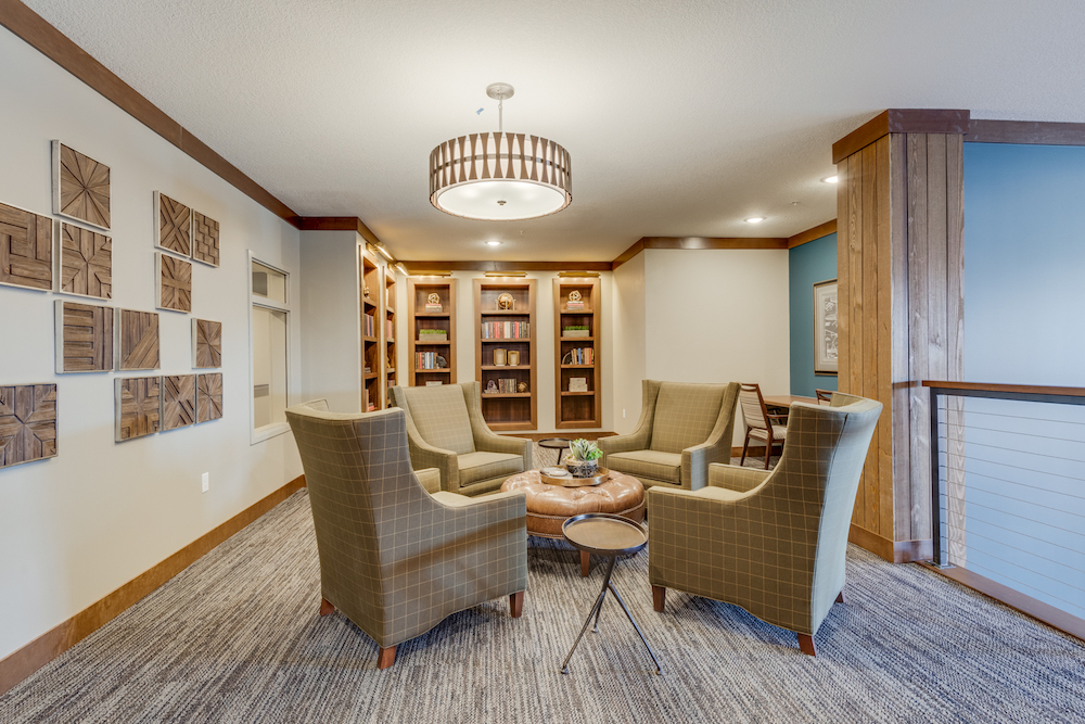 Cozy library with four armchairs around a round table, wooden bookshelves, and decorative wall art.