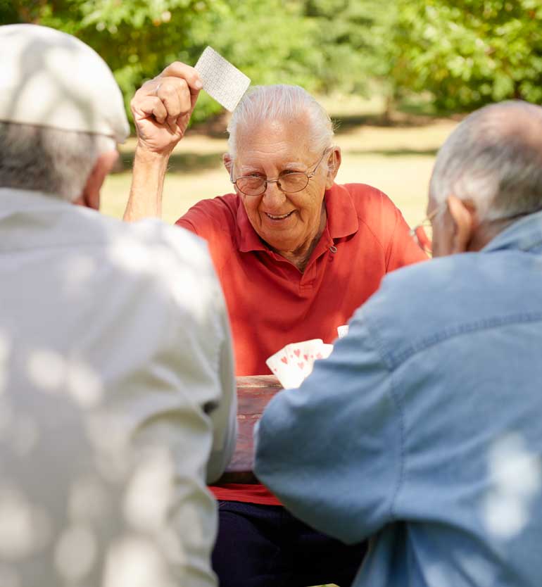 seniors-playing-cards Three elderly men enjoying a card game outdoors, with one holding up a card and smiling.