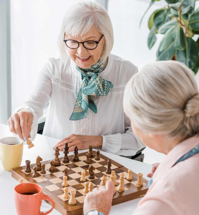 seniors-playing-chess Two elderly women enjoying a game of chess at a bright, modern space with coffee mugs on the table.