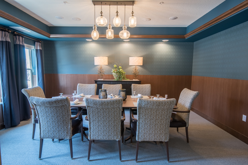A dining room with eight cushioned chairs, a wooden table, and modern overhead lighting fixtures.