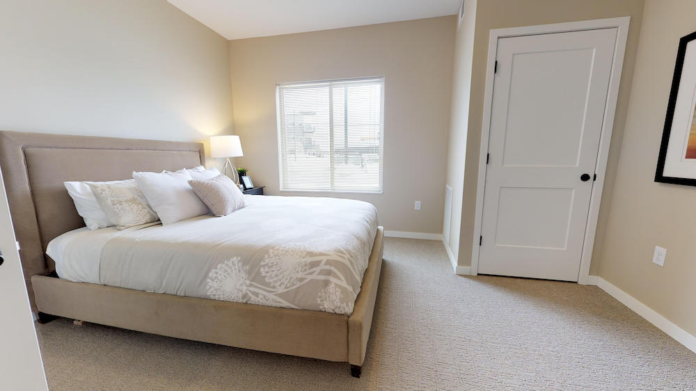 Model home bedroom with large bed, bedside lamp, window, and closed closet door.