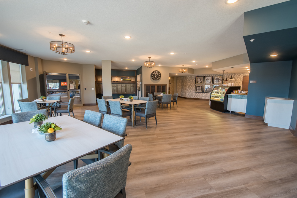 Modern communal dining area with large clock, various seating arrangements, and natural light.