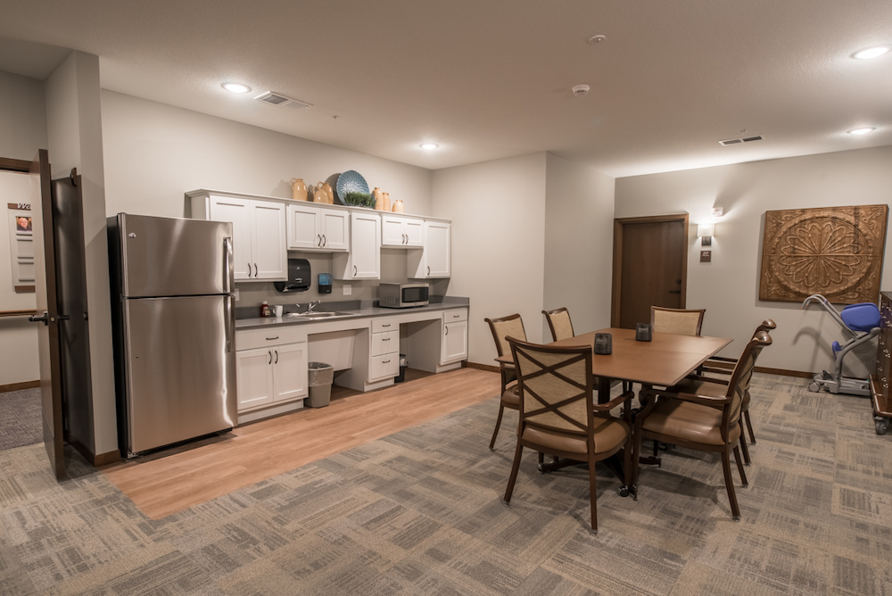 Modern communal kitchen area with stainless steel appliances, wooden table, and decorative wall art.