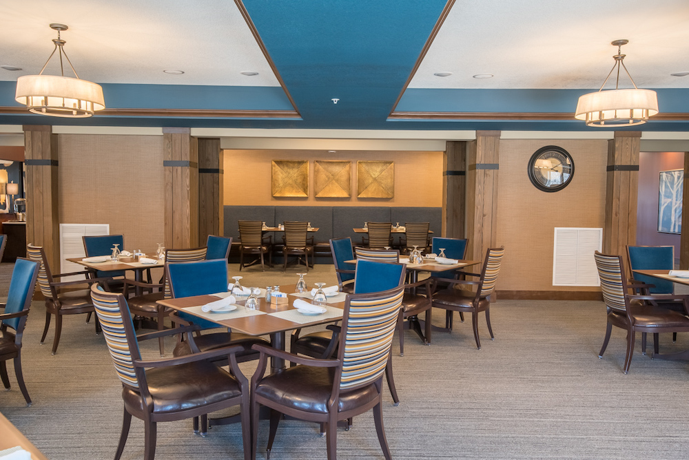 Modern dining room with wooden tables and striped chairs, blue accents, and pendant lighting.