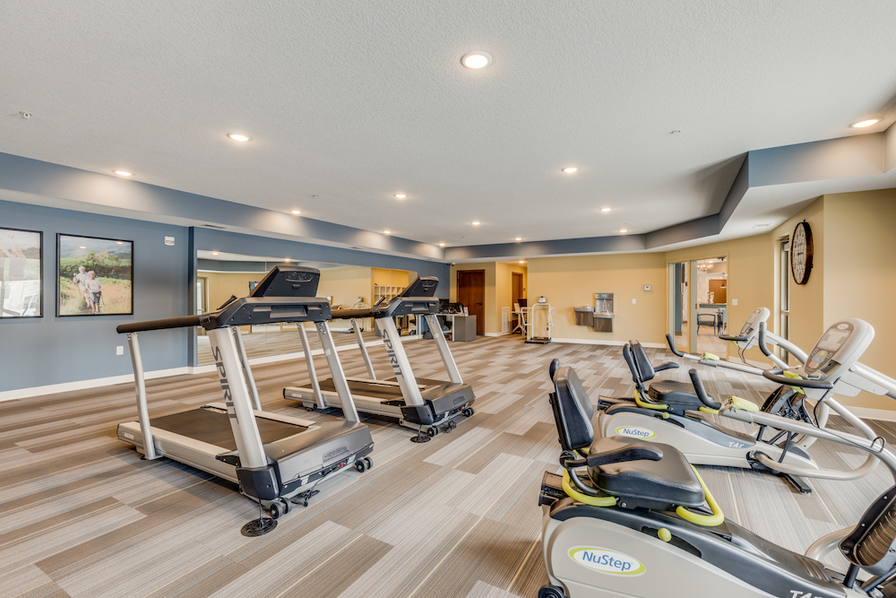Modern fitness center with treadmills and NuStep exercise machines, well-lit with recessed lighting.