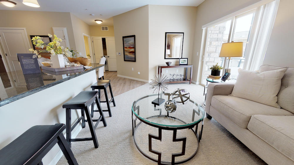 Spacious living room with modern decor, glass coffee table, beige sofa, and large windows.