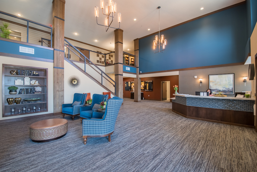 Modern lobby with wooden staircase, reception desk, blue chairs, and bookshelves