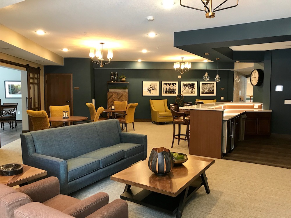 A modern lounge area featuring a large sofa, chairs, tables, and a kitchen with a counter and barstools.