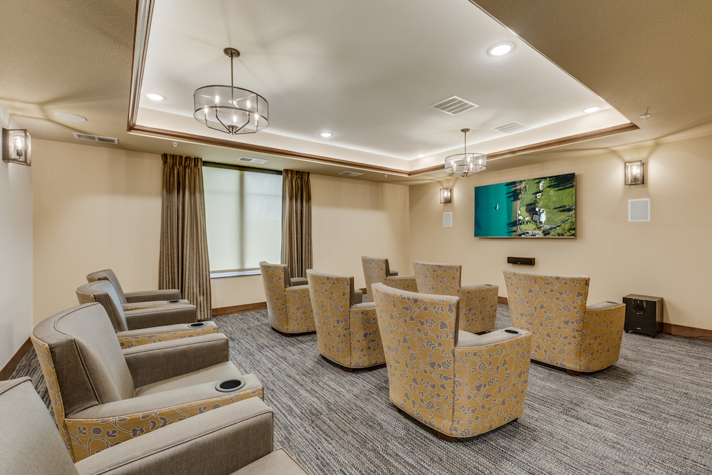 Small home theater room with beige and yellow seating, wall-mounted TV, and modern light fixtures.