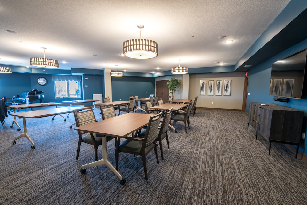 A spacious meeting room with wooden tables, chairs, modern lighting fixtures, and blue accent walls.