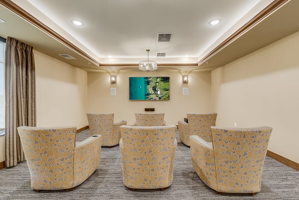 Bright lounge with six armchairs facing a large TV.